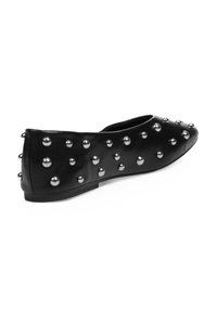 Zapato plano negro de cuero, con punta afilada y adornado con tachuelas metálicas en la parte superior y los lados. Suela simple y de bajo perfil.