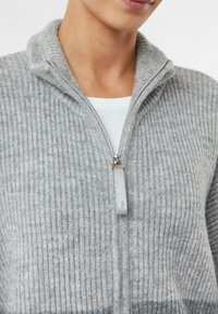 Helles graues Reißverschluss-Sweatshirt mit gerippter Struktur, ausgestattet mit einem hohen Kragen und einem silbernen Reißverschluss mit einem Stoff-Zippanhänger.