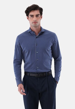 Camicia a maniche lunghe blu navy con strisce verticali bianche, colletto button-down e vestibilità slim, abbinata a pantaloni scuri e una cintura nera.