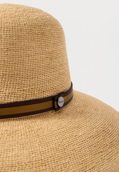 Μπεζ πλεκτό ψάθινο καπέλο με φαρδύ γείσο και καφέ-μουσταρδί ριγωτή κορδέλα με μικρό στρογγυλό ασημί λογότυπο.