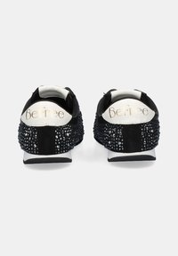 Zapatillas deportivas negras con parte superior de tela texturizada, adornadas con tachuelas metálicas en el talón, con detalles en blanco y un logo.