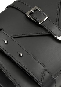 Černá kožená taška s texturovaným povrchem, s stříbrnou sponou, kontrastním stehem a dekorativními nýty po celé délce popruhu.