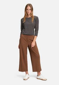 Pasiasta bluzka z długim rękawem w kolorze granatowym i kremowym, zestawiona z szerokimi brązowymi spodniami. Białe trampki z jasnobrązową podeszwą.