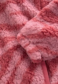 Fuzzy pink fleece fabric with varying shades, featuring a soft, textured surface and subtle color gradients. Edges are smooth and flexible.