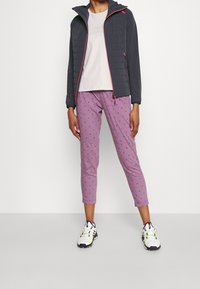 Veste matelassée gris foncé avec capuche, T-shirt gris clair, pantalon violet à motif, et chaussures de sport blanches avec des accents néon.