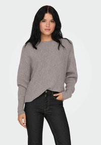 Lichtgrijze, geribbelde trui met een ontspannen pasvorm, ronde halslijn en lange mouwen, gecombineerd met donkerblauwe jeans met gele stiksels.
