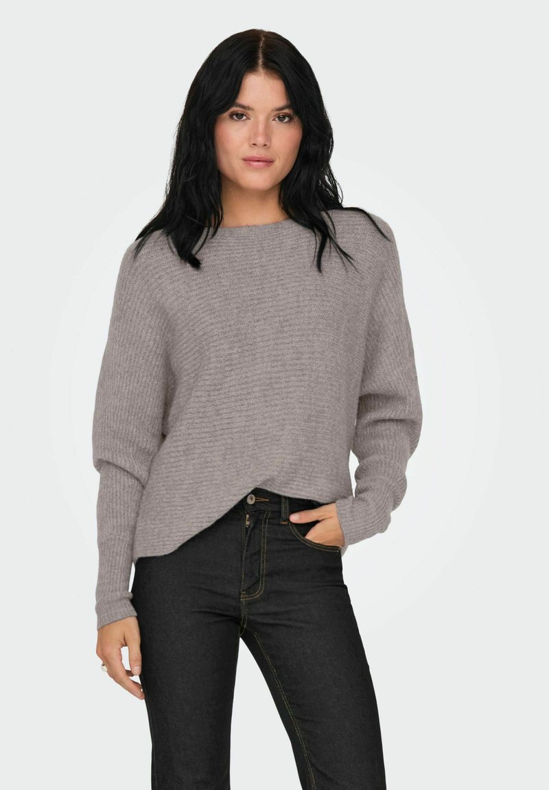 Lichtgrijze, geribbelde trui met een ontspannen pasvorm, ronde halslijn en lange mouwen, gecombineerd met donkerblauwe jeans met gele stiksels.