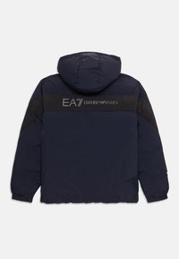 Jūros mėlynos pūkinės striukės su gobtuvu, ant pečių esantys juodi intarpai, kuriuose sidabrinė spalva užrašyta "EA7 Emporio Armani" logotipas.