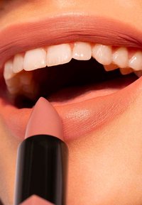Nude lipstick with a matte finish held near open lips, showcasing smooth texture and soft pink shade against a natural lip color.