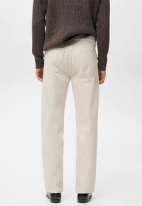 Pantalones beige de pierna recta hechos de algodón. Incluyen bolsillos traseros, costuras entalladas y una textura suave. Combinados con un suéter de punto marrón.