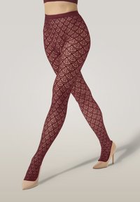 Benene er krydset, iført burgunderfarvede mønstrede tights og beige højhælede sko, som viser tekstureret design og tætsiddende talje.