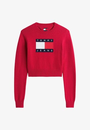 Czerwony sweter z dzianiny z ryflowanym obszyciem na dole i mankietach. Na środku znajduje się prostokątna naszywka z logo w kolorach granatowym, białym i czerwonym.