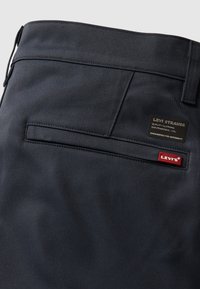 Pantalon Levi's bleu marine foncé montrant la poche arrière avec la languette rouge du logo Levi's et une étiquette noire avec le texte « Quality Clothing, San Francisco, Cal. »