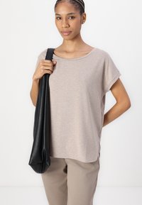 Beige, lett, kortermet topp med vid halsåpning, kombinert med beige bukser. En svart lærveske henger over den ene skulderen.