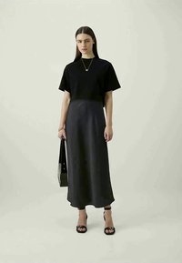 Top preto de mangas curtas combinado com uma saia longa de cetim escuro. A modelo usa sandálias pretas de tiras e segura uma mala tote preta.