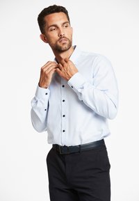 Lichtblauw overhemd met een textuurpatroon, zwarte knopen en contrasterende manchetten. Draag het met een donkere broek en een zwarte riem.