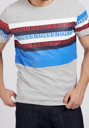 Gray short-sleeve T-shirt featuring horizontal stripes in blue, white, and dark red with repeated "GUESS" text. Smooth cotton material.