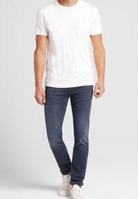 Vit t-shirt med kort ärm som matchar mörkblå jeans och vita sneakers. Enkel design, bekväm passform, inga synliga mönster eller detaljer.