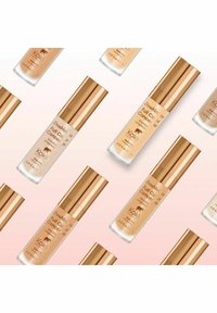 Kokie Double Duty Full Coverage Concealer i glasflasker med guldmetallic kapsler. Nuancer spænder fra lys beige til varm tan, med mærkning fra brandet.