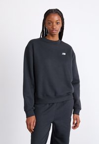 Sweatshirt noir en mélange de coton avec un col rond, des poignets et un ourlet côtelés, présentant un petit logo blanc sur la poitrine gauche.