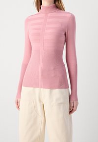 Pull à col roulé rose avec texture à rayures verticales, poignets et ourlet côtelés, coupe ajustée, matière douce. Assorti à un pantalon de couleur claire.