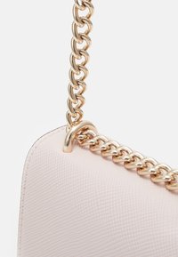 Rodblossrosa handväska med texturerad yta, utrustad med en guldkedjerem och en slät yta längs den övre kanten, med en metallisk detalj.