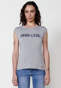 Sivi kratki rukav T-shirt s okruglim izrezom, s natpisom "FEAR-LESS" izraženim u mornarskim kristalima. Mekana tkanina s opuštenim krojem i zakrivljenim rubom.