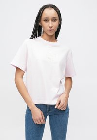 Απαλό ροζ βαμβακερό t-shirt με στρογγυλή λαιμόκοψη, κοντά μανίκια και μικρό αντανακλαστικό λογότυπο στο μπροστινό μέρος. Συνδυάζεται με μπλε τζιν παντελόνι.