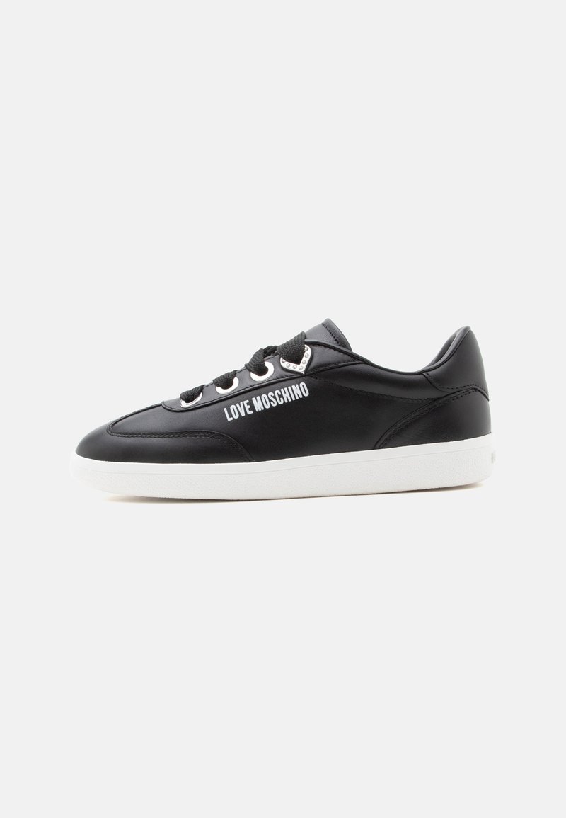 Baskets noires Moschino avec semelle blanche, lacets noirs et œillets argentés en forme de cœur sur un fond uni clair.