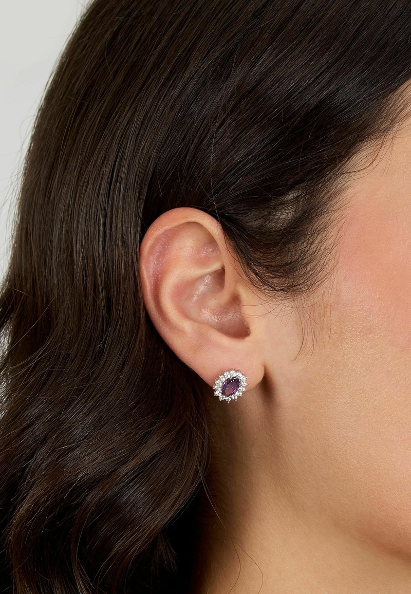 Orecchini in pietra preziosa viola montati in argento con un alone di piccole pietre trasparenti, caratterizzati da una forma ovale e una superficie lucida, sospesi dal lobo dell'orecchio.