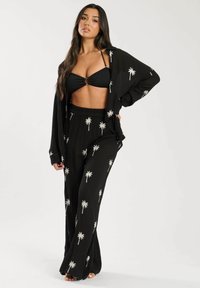 Completo nero in due pezzi composto da un top bikini con scollatura a halter e pantaloni ampi con una fantasia di palme bianche. Il tessuto ha una finitura testurizzata.