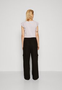 Haut léger à manches ondulées de couleur violet clair associé à un pantalon cargo large noir avec des poches latérales et une taille élastique.