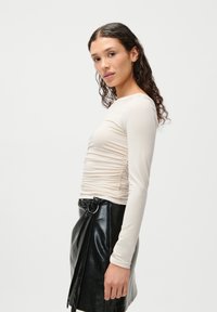 Długi rękaw kremowy top o teksturze marszczonej, w zestawieniu z wysokim czarnym spódnicą z ekologicznej skóry z pętlą na pasek i detalem w postaci wiązania.