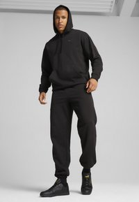 Sort hætte sweatshirt med en frontlomme og matchende sweatpants, parret med sorte sneakers med gule accenter. Glat stoffets tekstur.