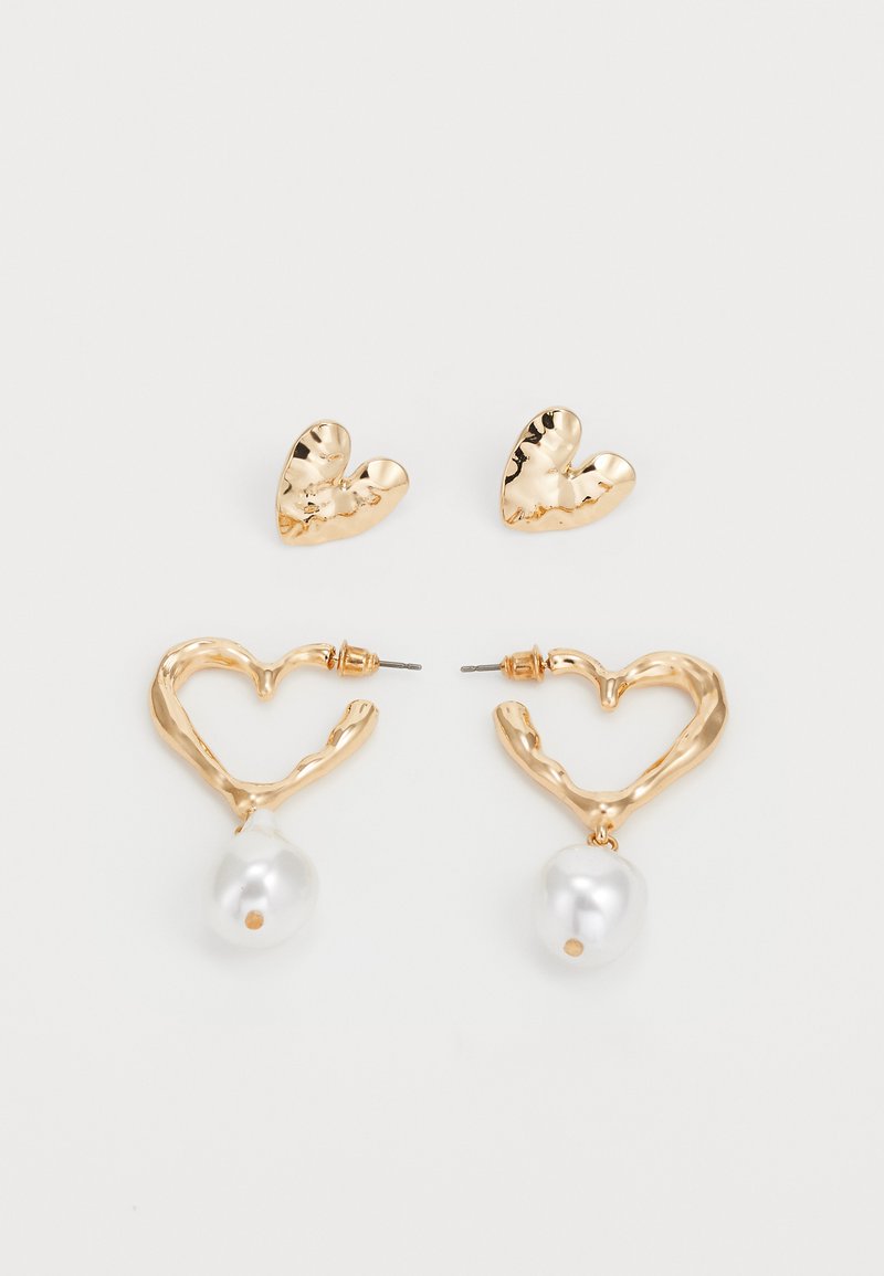 Pendientes en forma de corazón en tono dorado con un acabado texturizado, que cuentan con un colgante de perla. Incluye pendientes de stud en forma de corazón a juego.