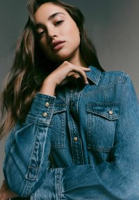 Denimjacka med två bröstfickor, detaljer i silverknappar och en avslappnad passform. Tyget har en strukturerad yta och är i medelblå färg.