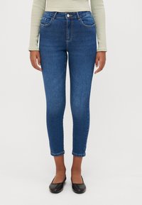 Jeans de mezclilla azul con corte ajustado, cintura de media altura y longitud recortada. Presentan un diseño clásico de cinco bolsillos y un ligero desgaste que añade textura.