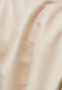 Tissu beige clair à texture lisse, présentant un tissage fin et un léger éclat, drapé doucement pour exposer ses plis.