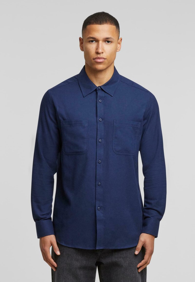 Camisa de manga larga azul marino con botones en el frente, cuello puntiagudo, dos bolsillos en el pecho y un acabado textil suave. Ligera y de corte entallado.