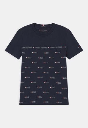 Navy blue cotton t-shirt featuring repeated "Tommy Hilfiger" logo in white with red and blue accents. Classic crew neckline and short sleeves.