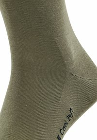 Chaussette verte olive présentée, avec une texture côtelée et un talon renforcé. Un texte noir près de la cheville indique : "Cool 24/7."