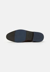Braune Schuhsohle mit blauen Gummiakzenten, strukturiertem Grip-Muster und einem glatten schwarzen Abschnitt an der Ferse mit Detail des Markenlogos.