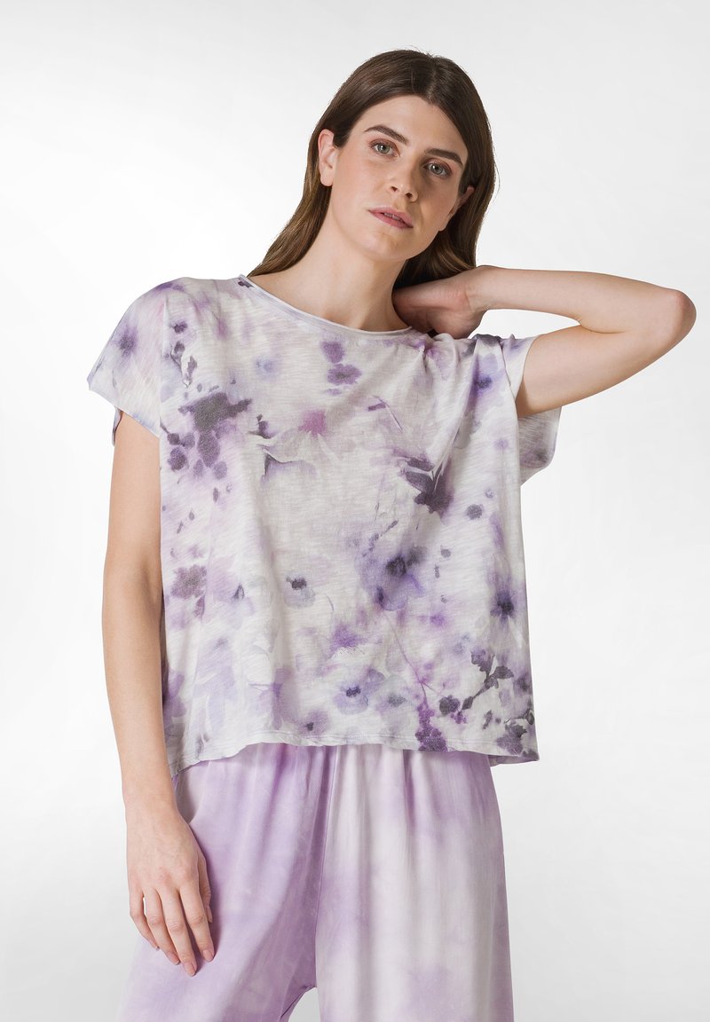 Top ligero de manga corta en un patrón de tie-dye blanco y lavanda, con un ajuste holgado y una textura suave, combinado con pantalones a juego en lavanda.