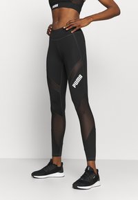 Svarta atletiska leggings med nätpaneler, figurnära design och Puma-logotyp i vitt på låret, i kombination med svarta löparskor.