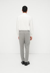Γκρι παντελόνι με άνετη εφαρμογή, ελαστική μέση και διακριτική λεπτομέρεια στην πίσω τσέπη, σε συνδυασμό με λευκό πουκάμισο μακρυμάνικο.