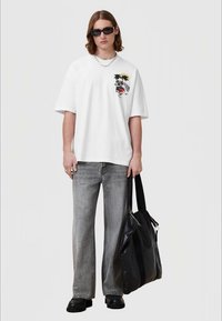 White oversized T-shirt with graphic of a tiger; paired with gray wide-leg jeans and black leather bag; model wearing black sunglasses.