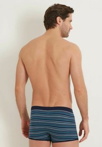 Blårandiga boxerkalsonger tillverkade av mjuk bomullsblandning, med ett marinblått midjeband och vertikala ränder i varierande nyanser av blått och grått.