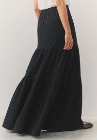 Czarna, warstwowa długa spódnica z teksturowanej tkaniny, z elastycznym paskiem w pasie. Charakteryzuje się zwiewną sylwetką, warstwową konstrukcją oraz delikatnymi falbankami.