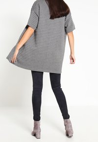 Överdimensionerad grå stickad tunika med ribbad textur, korta ärmar, kombinerad med mörka leggings och ljusgrå ankelstövlar.