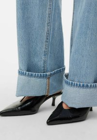 Jeans de mezclilla azul claro de pierna ancha con puños doblados, combinados con tacones puntiagudos de charol negro con un diseño recortado.